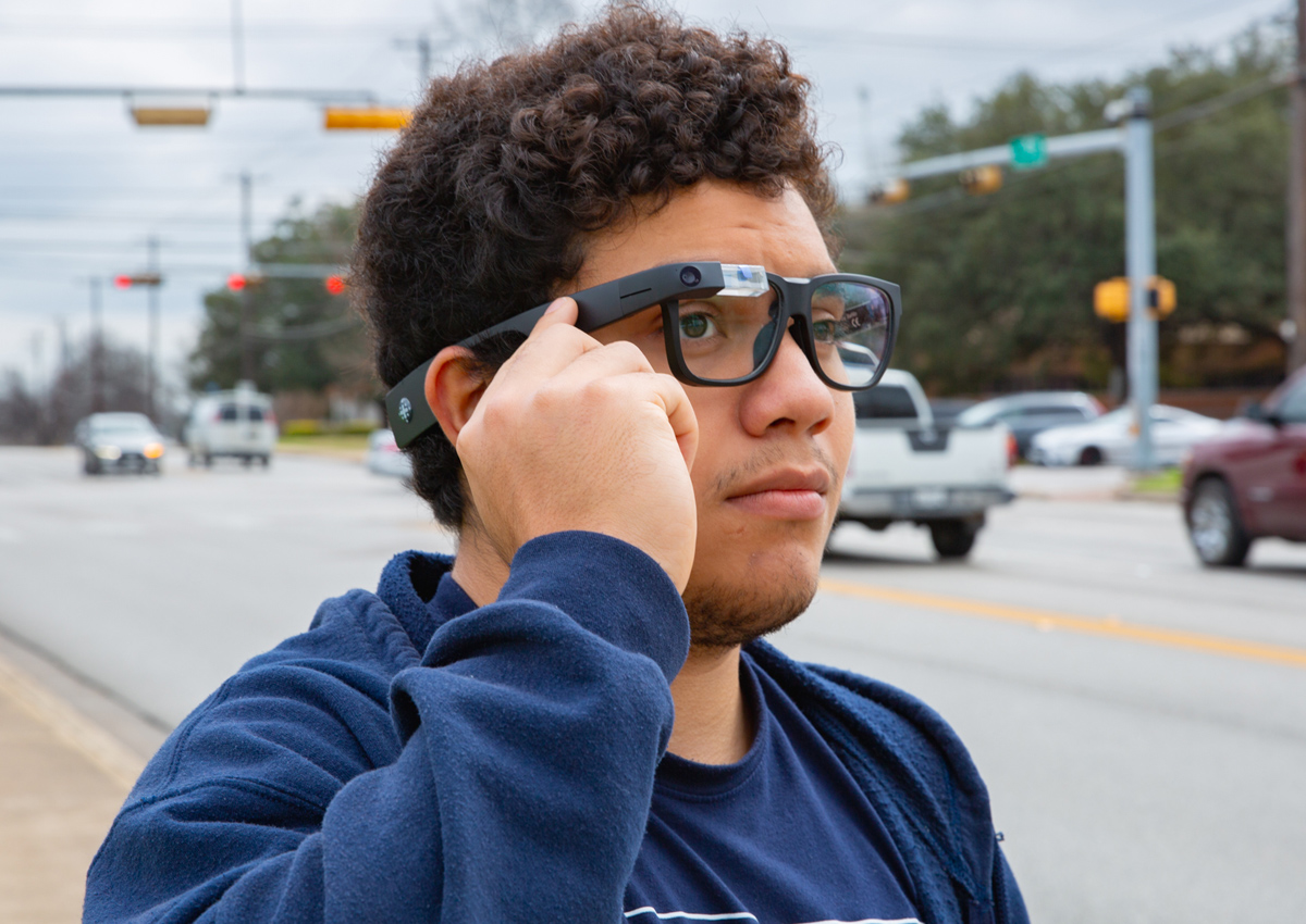 An adolescent taps the right side of the frame of his Envision glasses