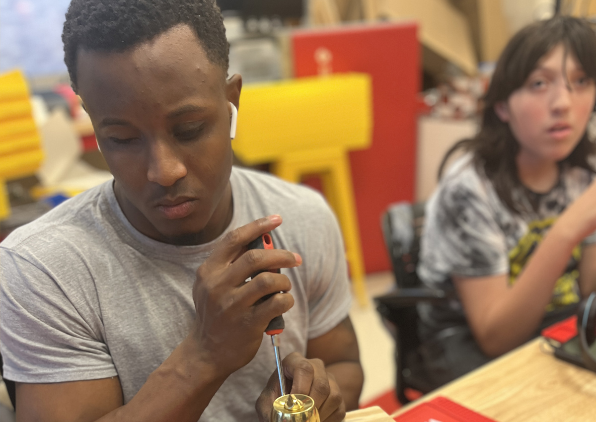 An adolescent uses a screwdriver to attach a doorknob to a wooden board.