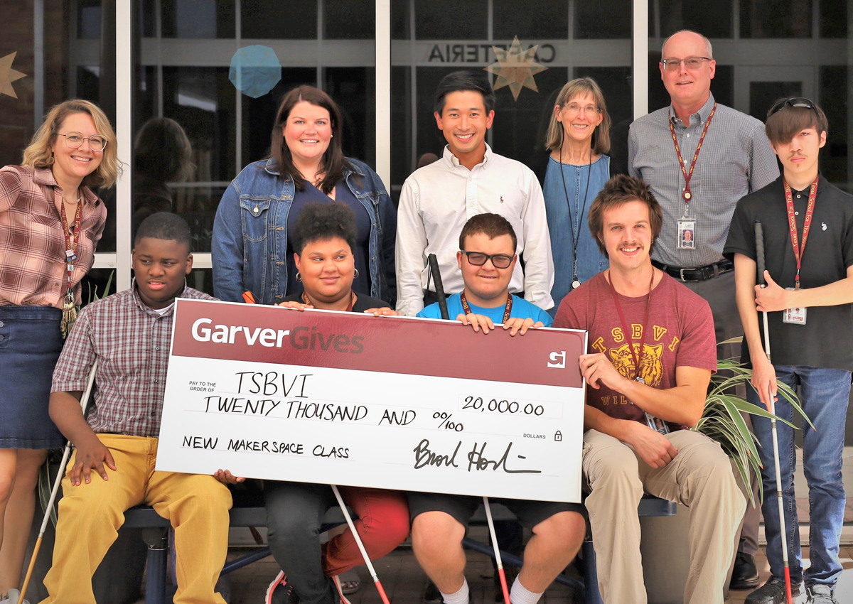 Six adults and four adolescents pose with an oversized check for $20,000 written by GarverGives to TSBVI for a new Makerspace.