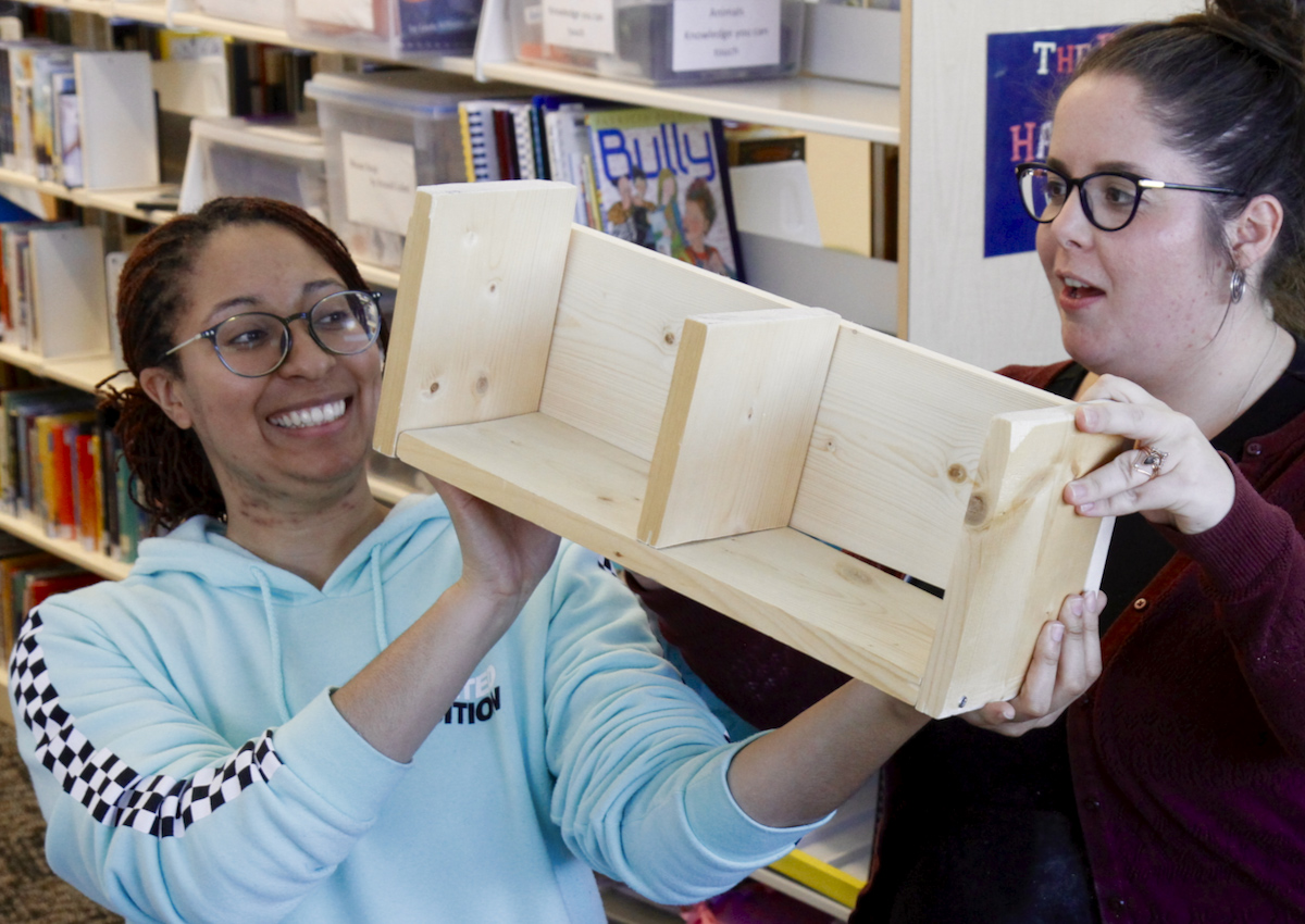 Two adults hold up a wooden sequence box in a library.