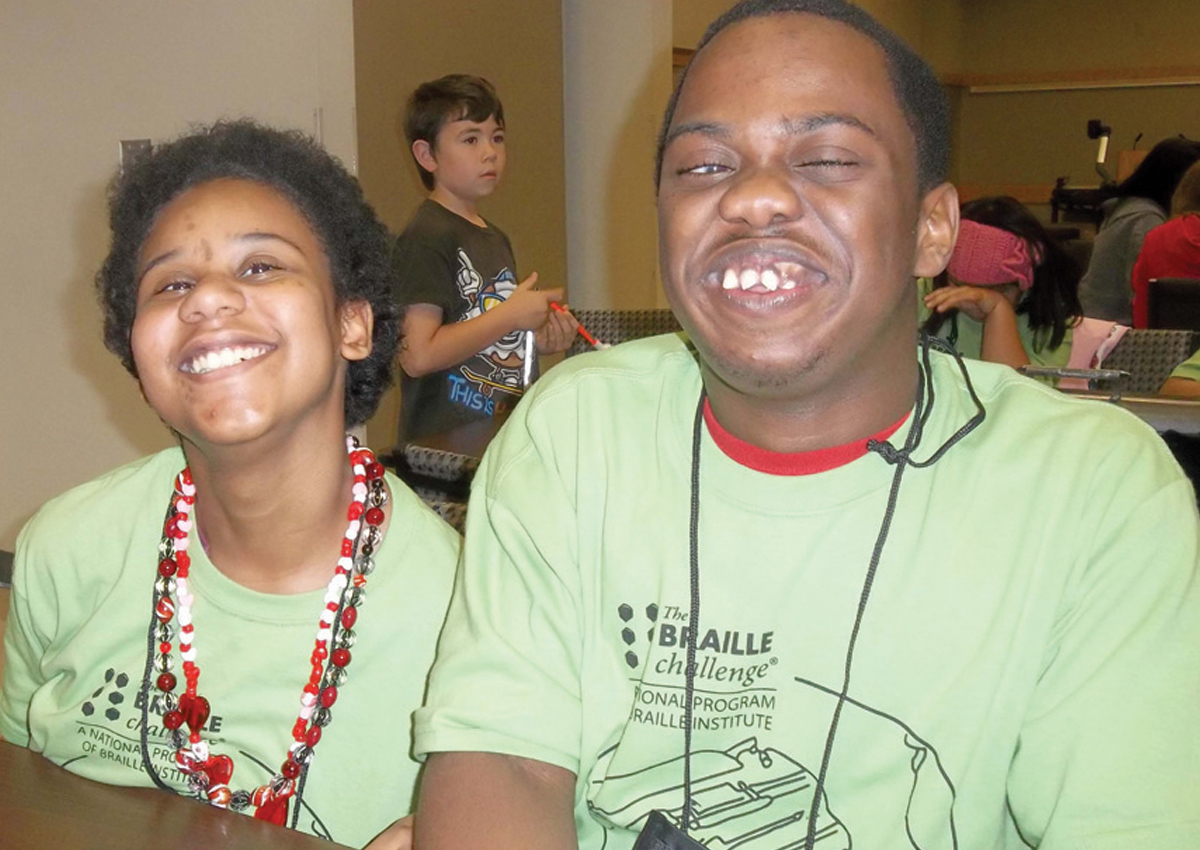 Two adolescents smile wearing matching green Braille Challenge shirts.