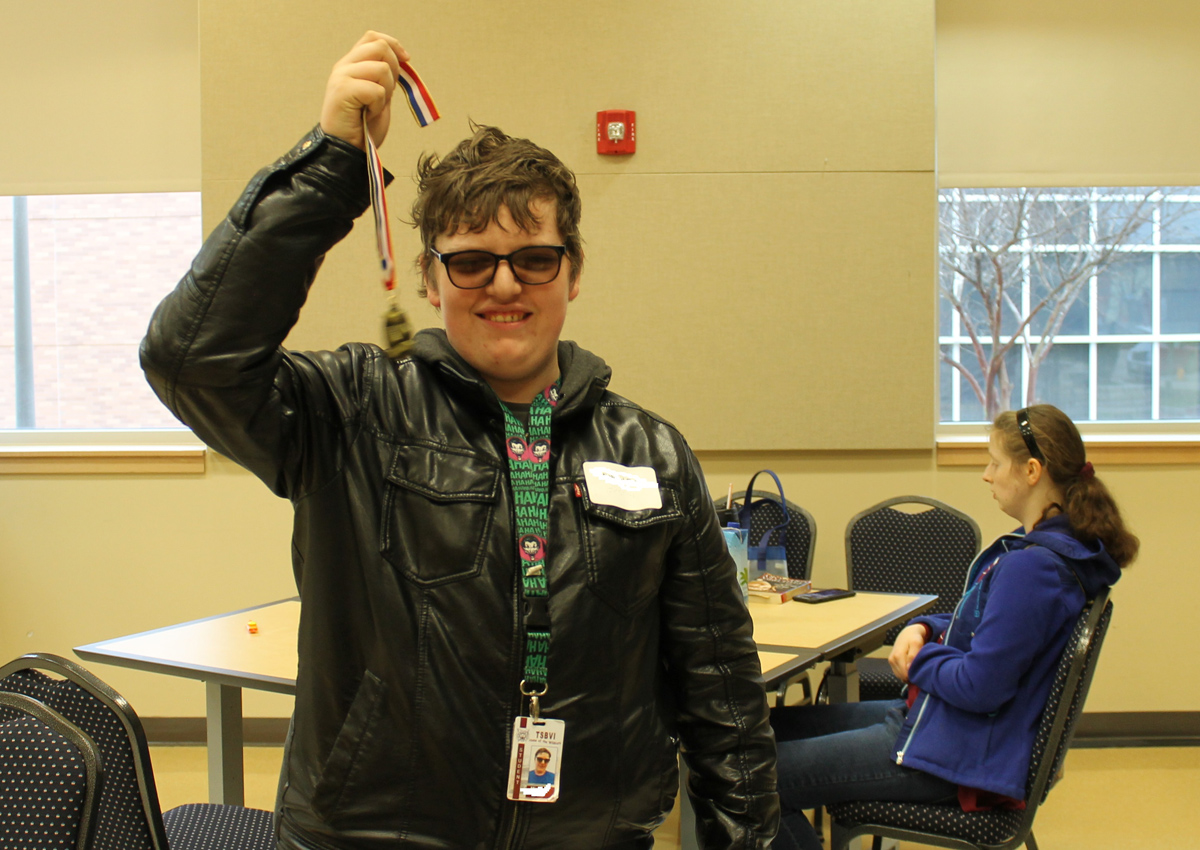 An adolescent proudly holds up a medal.