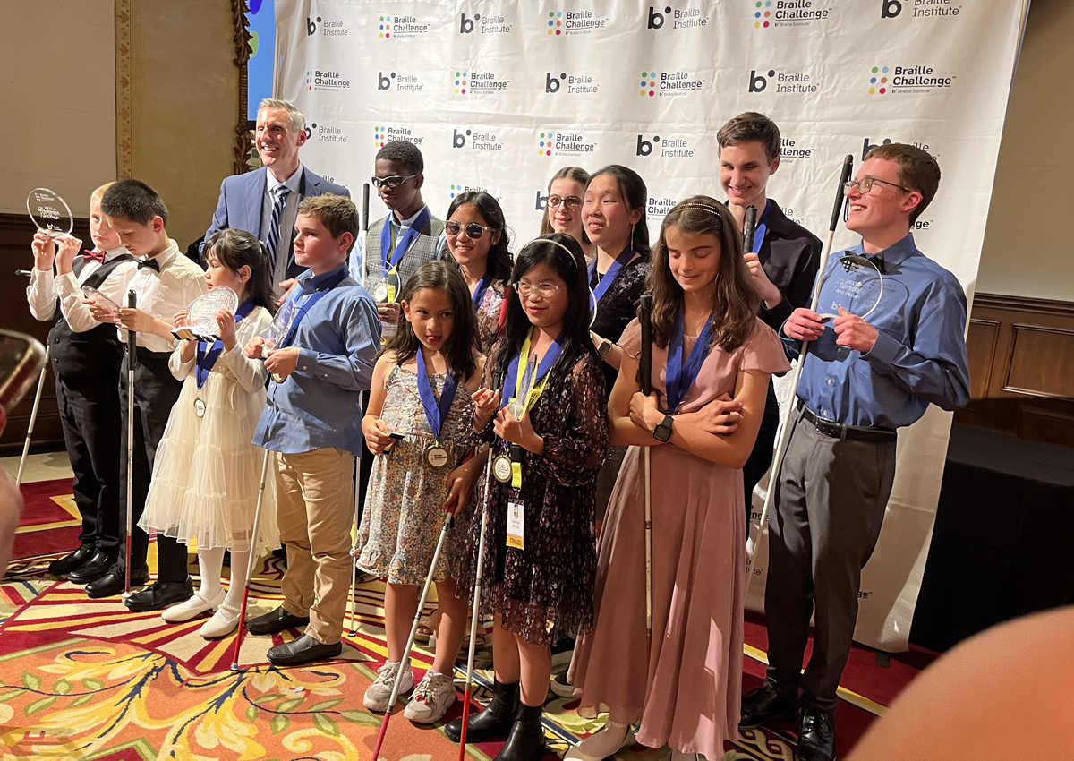 Adolescents dressed up wear medals and hold awards in front of a backdrop that reads 