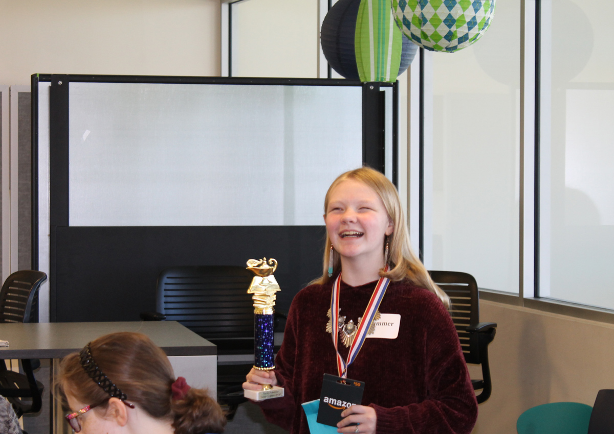 An adolescent smiles while holding a trophy.