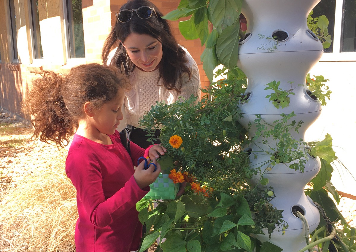 An elementary student and adult explore plants growing out of planter that grows plants in a four square foot vertical space.
