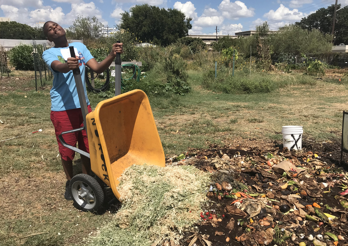 A secondary school-aged student dumps comport into a plot of land at a community garden.