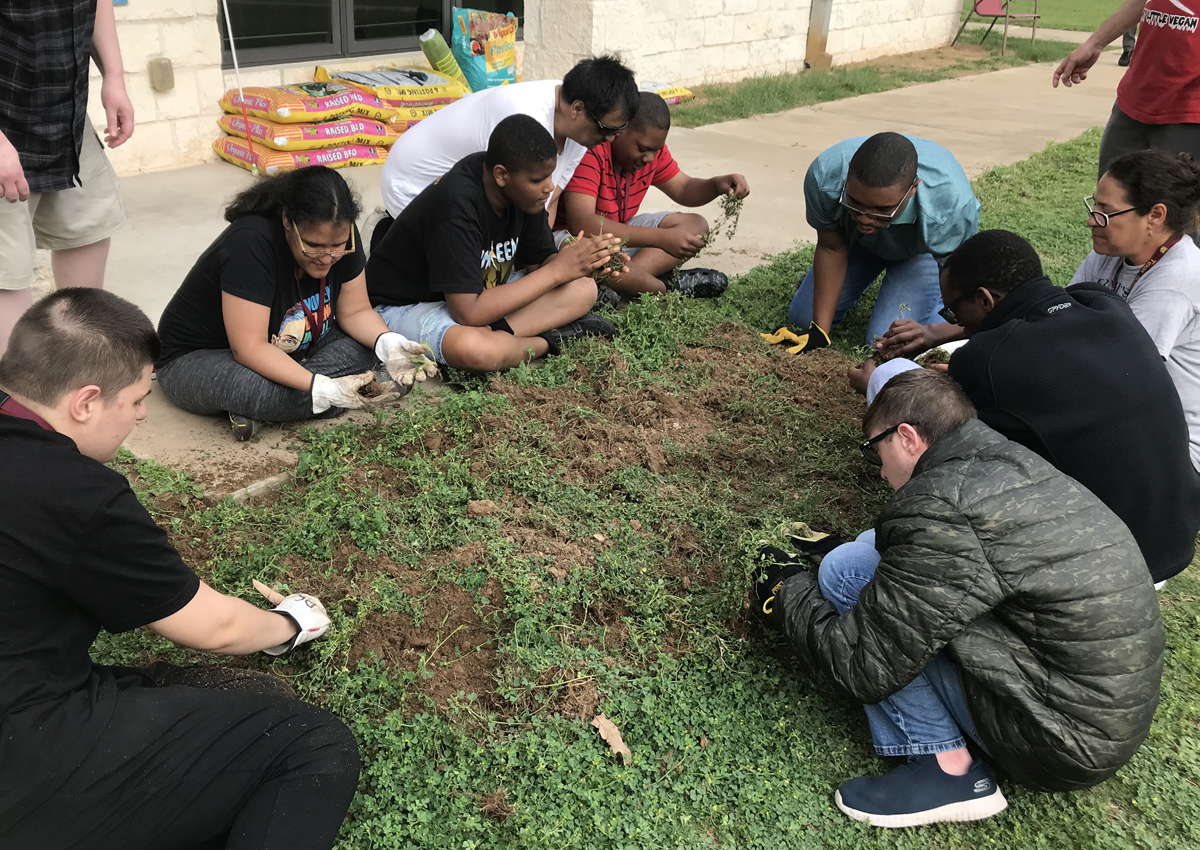 Adolescents and adults work together to clear a garden plot outside.