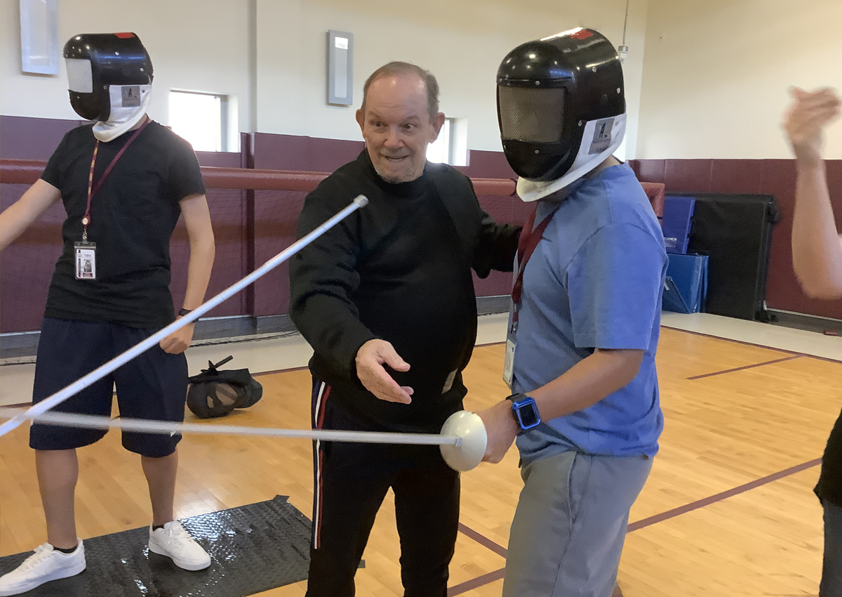 An adult guides adolescents using fencing foil sword.