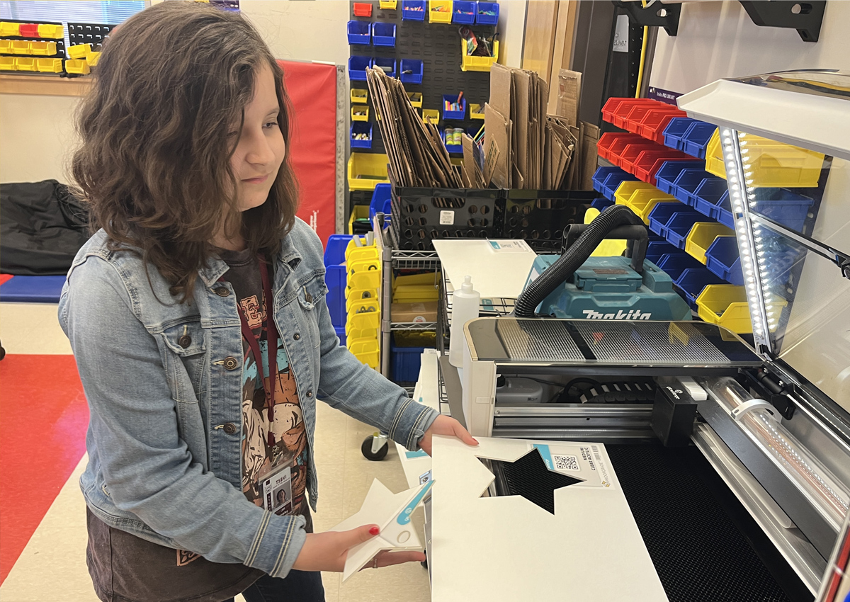 An adolescent holds up a star cut from acrylic printing material by a laser cutter.