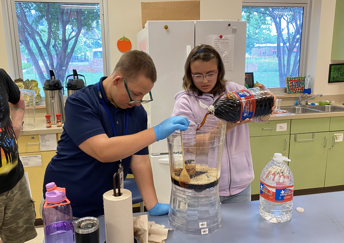 Two adolescents pour cold brew from a gallon jug into a thermos.