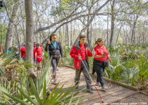 Adolescents and adults in matching red shirts use straight canes to hike along a trail in Palmetto State Park. Photo credit: Courtesy Maegan Lanham, TPWD