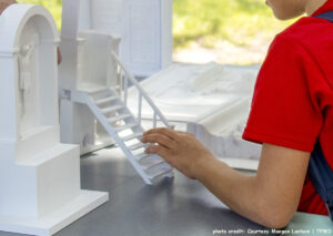 An adolescent’s hand feels the model steps of a chapel set on a table. A 3D replica of Jesus on a cross is on the table. Photo credit: Courtesy Maegan Lanham, TPWD