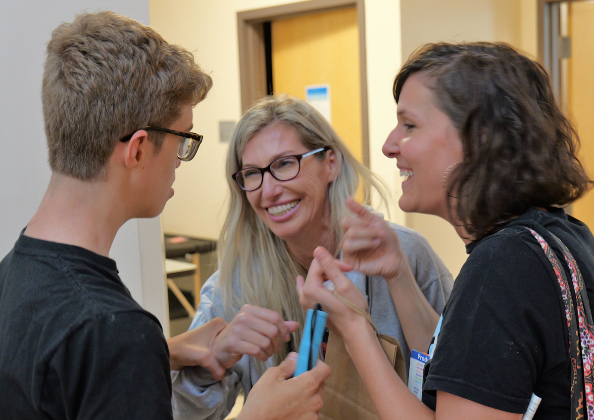 An adult uses American Sign Language to have a conversation with an adolescent who is gripping the arm of another adult.