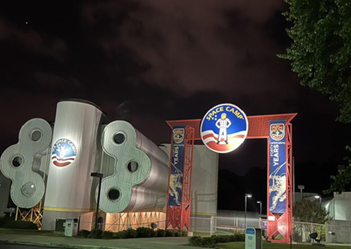The entry to Space Camp features a large labeled sign next to the habitat dorms, a metal structure of horizontally stacked cylinders around a taller vertical structure.