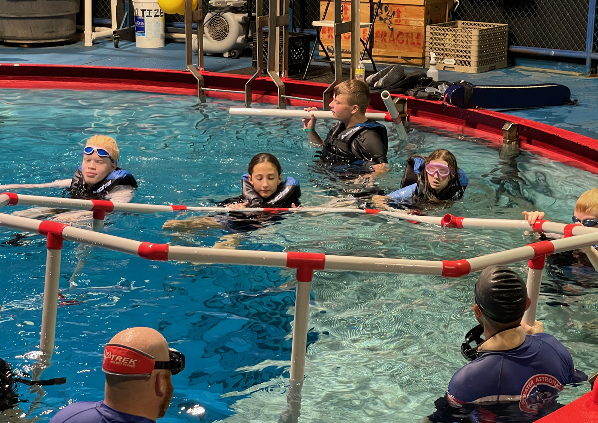 Adolescents in a pool work together to assemble large PVC pipes in an octagon-shape.