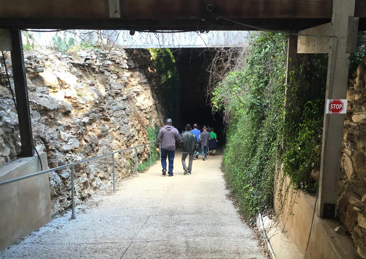 Adults and adolescents walk down a long ramp into the entrance of a cave.