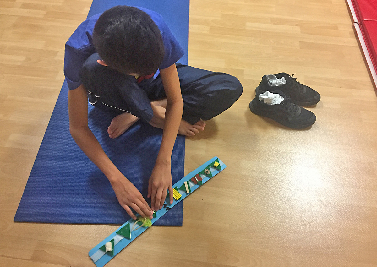 An adolescent sitting on a yoga mat reads a strip with 9 tactile symbols.