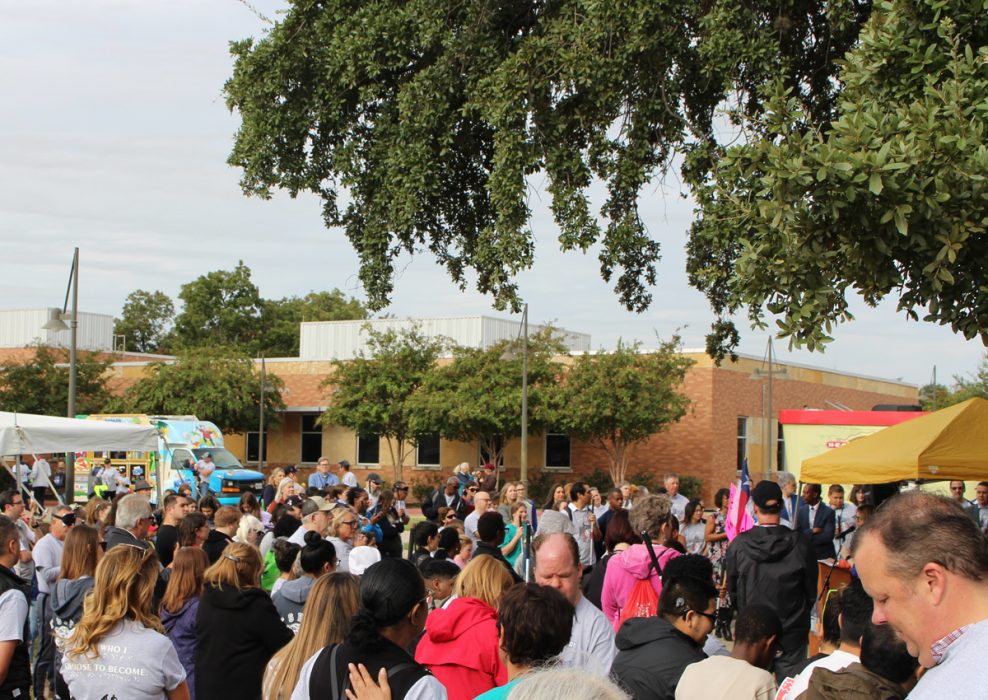 A crowd of people gather on a grassy lawn with a snow-cone truck and tents set up.