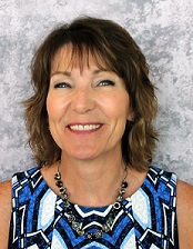 Photo fo TSBVI board member Brenda Lee. She is wearing a blue patterned shirt and standing in front of a grey background. She is smiling.