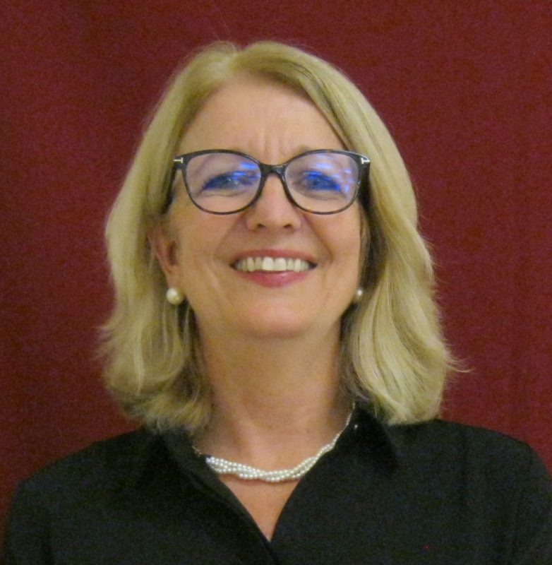 Photo of TSBVI board member Elaine Robertson, she is standing in front of a red background and smiling.