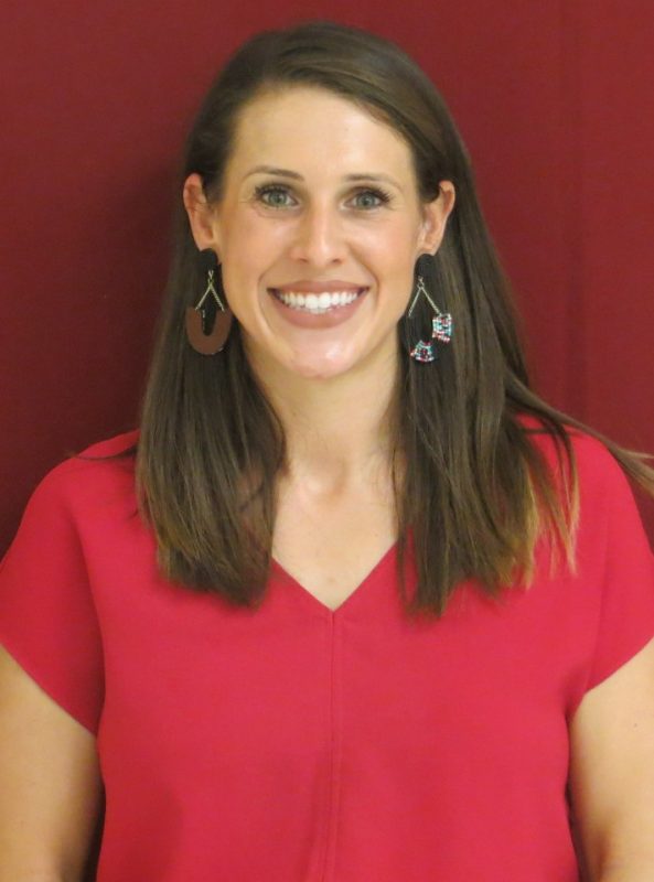 Photo of TSBVI board member Megan Gautney wearing a red shirt and standing in front of a red background and smiling.