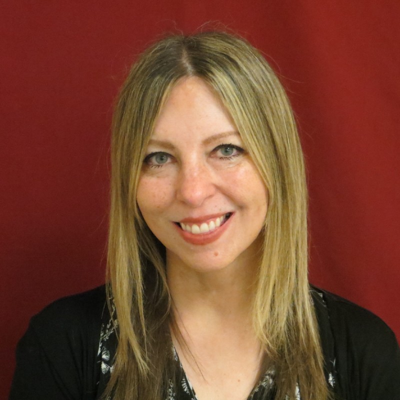 TSBVI Board member Belinda Rudinger wearing a black sweater and standing in front of a maroon background