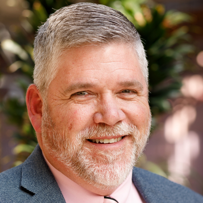 Photo of TSBVI board member Lee Sonnenberg. He is wearing a suit and standing in a backyard. He is smiling.