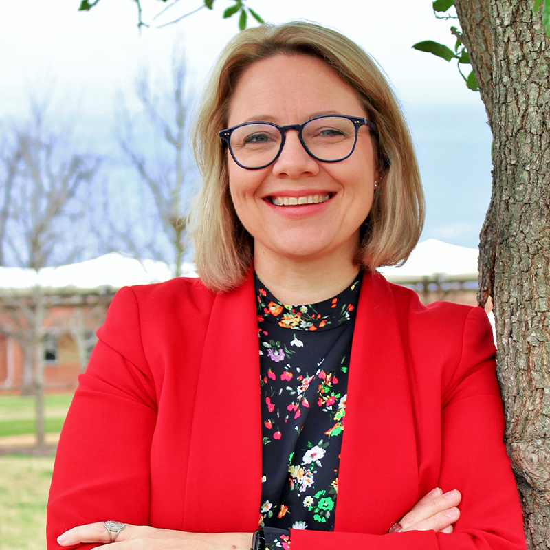 Superintendent Emily Coleman leaning on tree with arms crossed smiling