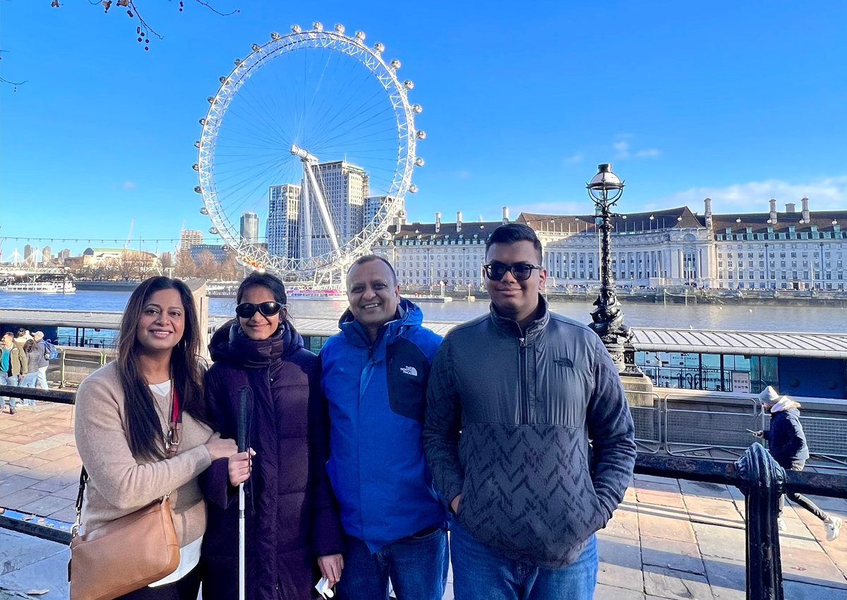 Cuatro adultos posan frente al río Támesis con el London Eye, o la Rueda del Milenio, al otro lado del río.