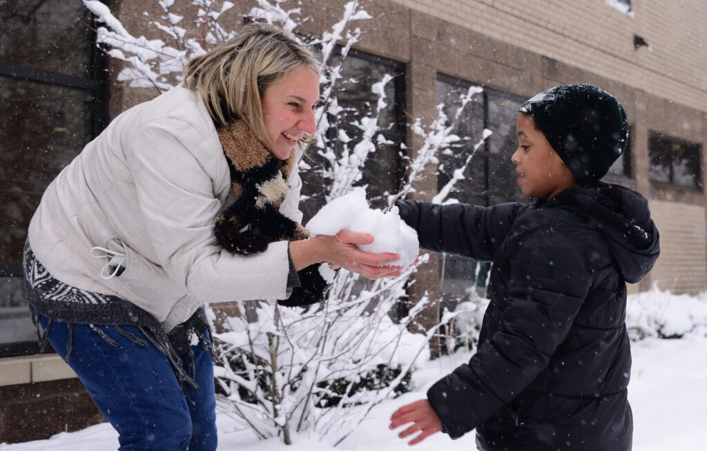 Teacher with a student exploring snow through touch and active learning strategies.