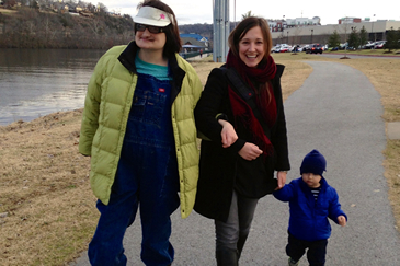 two adults in jackets walking, one is holding a baby's hand