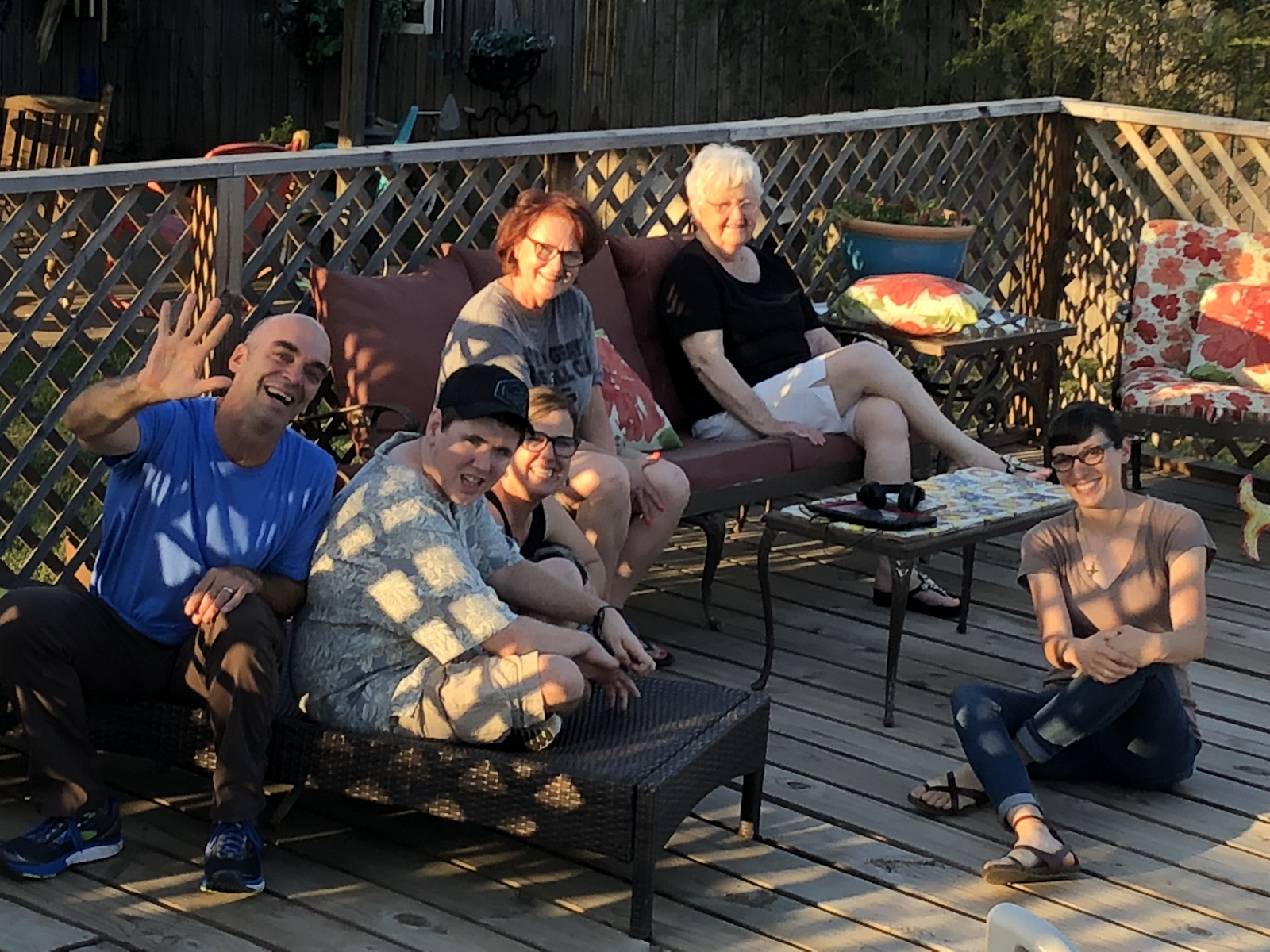 Six people sitting on lawn chairs outside and smiling. One person is waving to the camera.