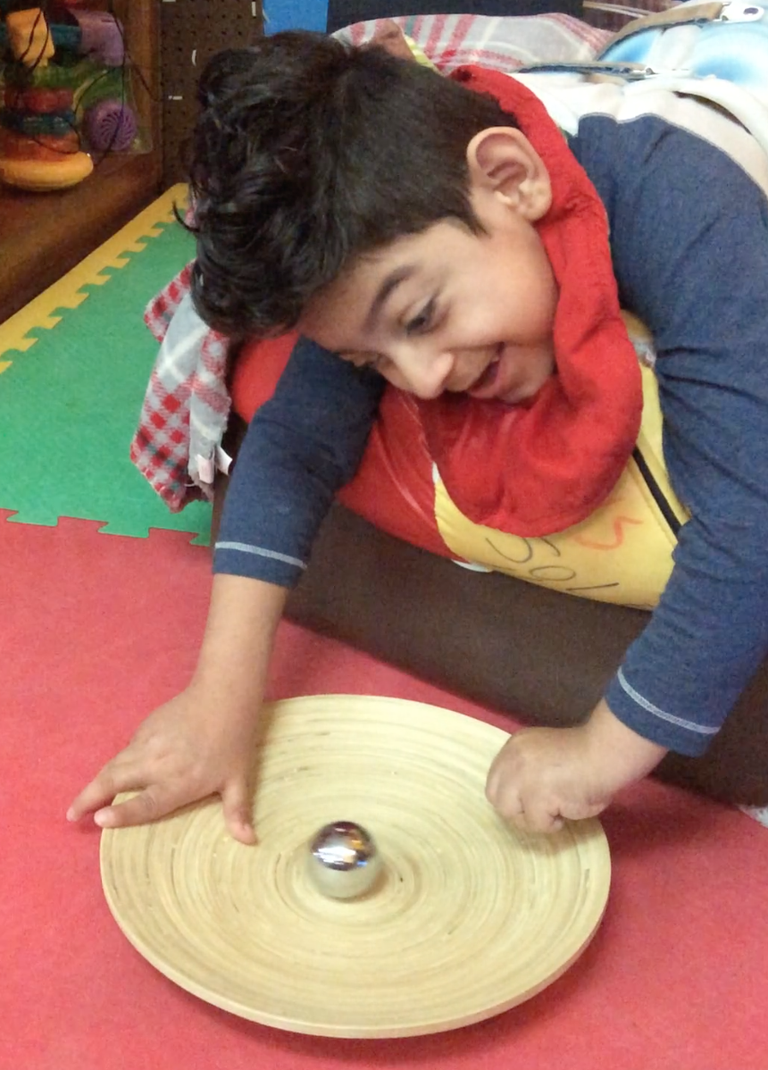 Student smiles as he plays with a metal ball on a tray.