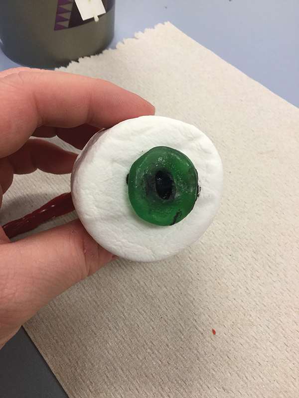 Photo closeup of a hand holding a giant marshmallow with a green gummy lifesaver attached to it.