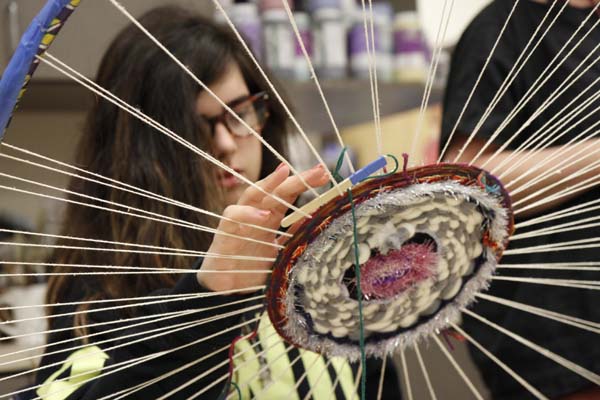 A young woman is shown behind a large, circular weaving.