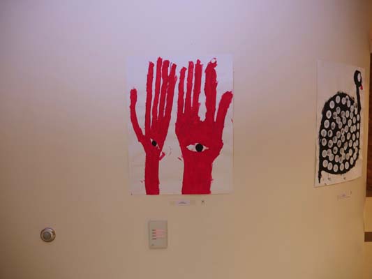 Painting of two red hands, reaching upwards, with eyes in the palms, on a white background.