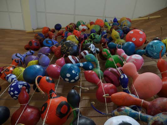 A number of painted gourds are strung together and hung from a rod to form a colorful curtain.
