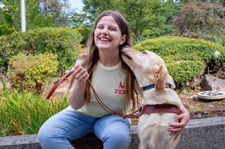 A yellow lab licks the face of a young student with long brown hair.