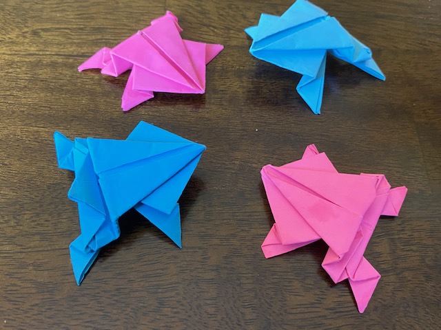 Four origami frogs made with pink and turquoise paper sit on a table. 