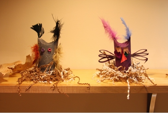 Two cardboard owls with feathers in nests of shredded paper