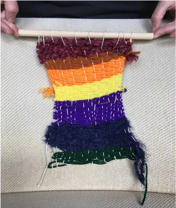 A colorful weaving hangs on a wooden dowel.