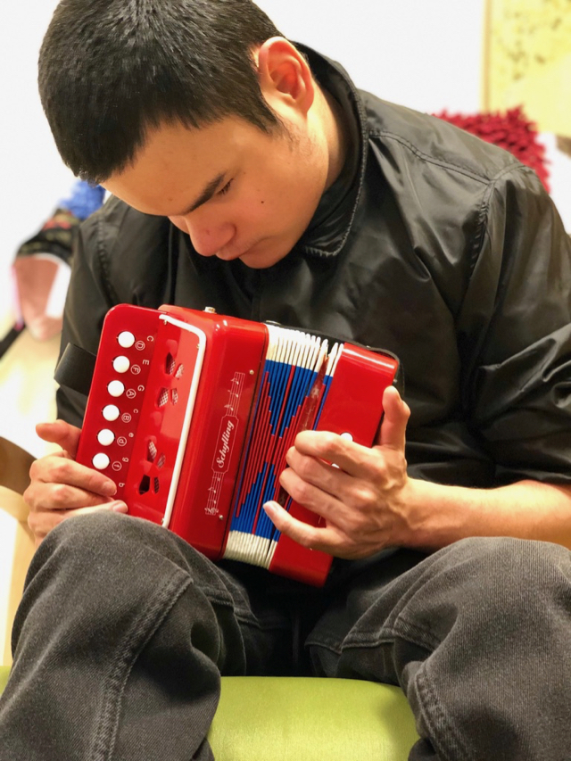  An adolescent TSBVI student has both hands on a red, white and blue accordion. The student’s right hand pushes the white keys.  