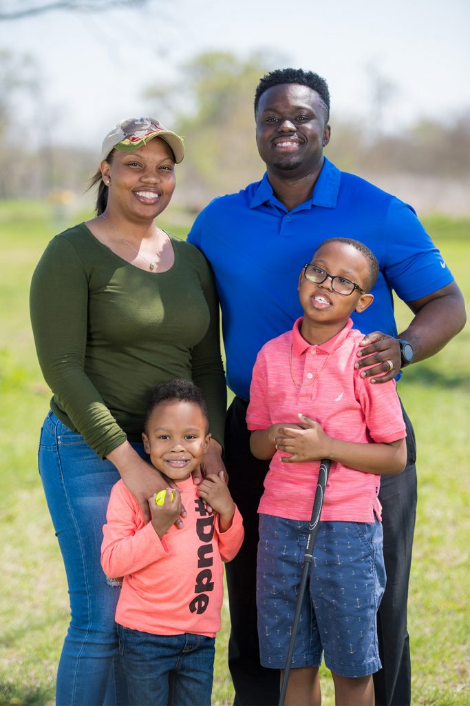 An elementary school-aged student holding a cane poses outside with parents and a sibling.