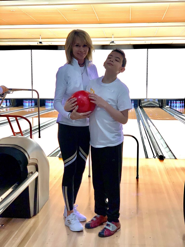 Aidan and Sherry hold a red bowling ball together during bowling activities at Special Olympics.