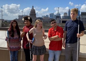 Five students, four of them holding canes, lean against a low wall.