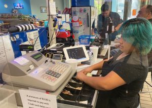 A student with shoulder length blue hair puts money into a cash register.