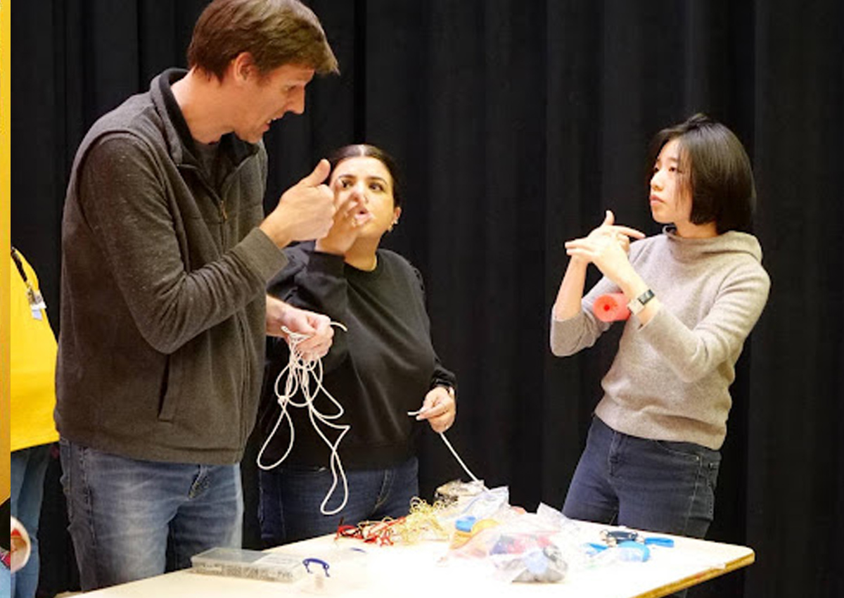 Three teachers sign to each other as they stand around a table of Active Learning materials.