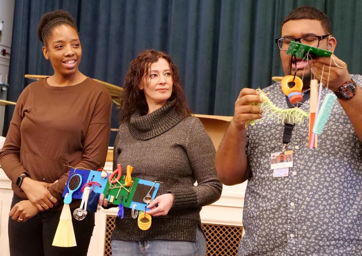 Three teachers stand in front of a school stage and show the Active Learning materials their team created.