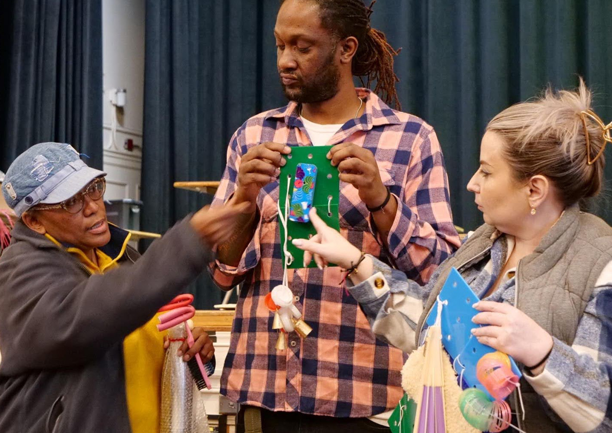 Three teachers, standing in front of the school stage, show each other the Active Learning materials they created.