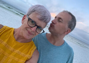 Julia and her brother, Bobby standing on a beach. Bobby’s face is turned toward Julia with lips puckered while Julia smiles at the camera.